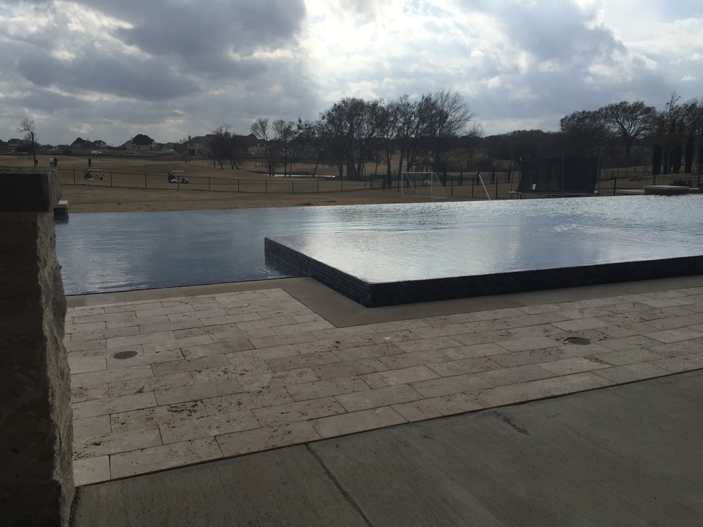 Idées déco pour une grande piscine arrière et à débordement moderne rectangle avec des pavés en pierre naturelle et un bain bouillonnant.