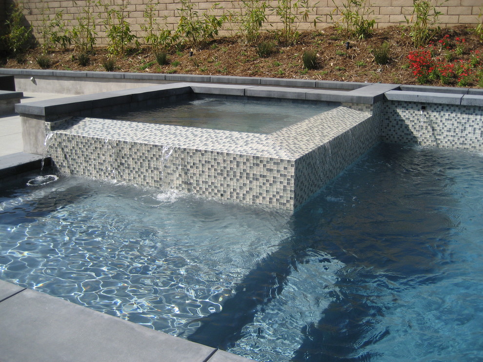 Ejemplo de piscina con fuente elevada de estilo zen de tamaño medio rectangular en patio trasero con losas de hormigón