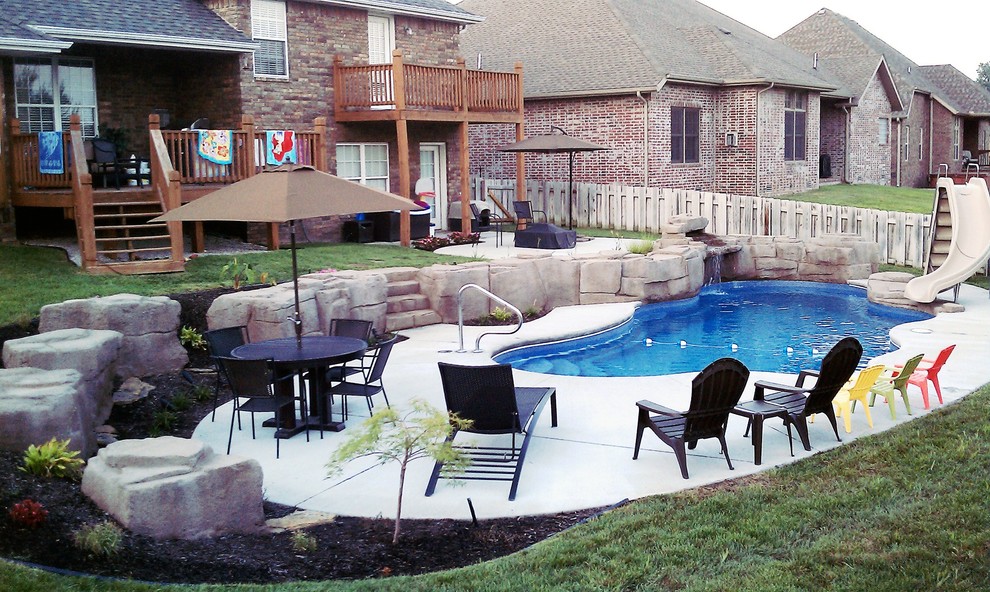 Imagen de piscina con tobogán natural rural grande a medida en patio trasero con suelo de hormigón estampado