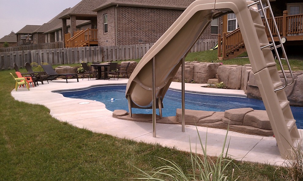 Идея дизайна: большой естественный бассейн произвольной формы на заднем дворе в стиле рустика с водной горкой и покрытием из декоративного бетона