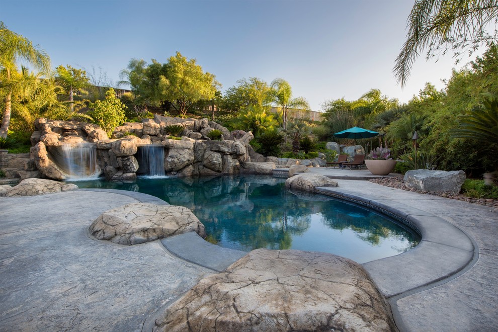 Imagen de piscina con fuente natural exótica grande a medida en patio trasero con losas de hormigón