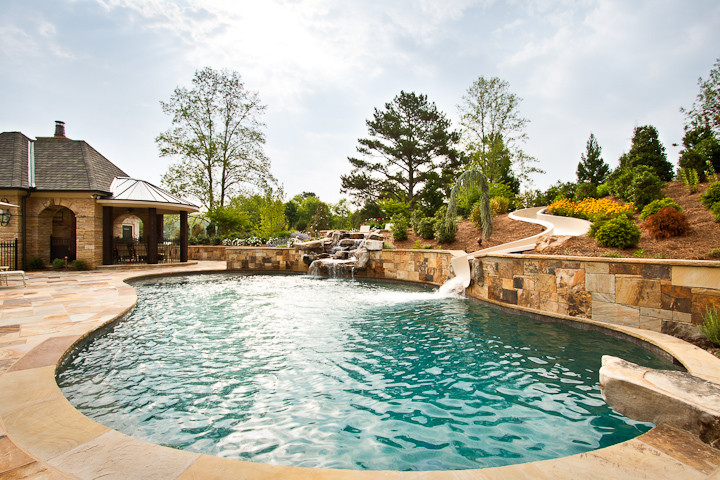 Esempio di una grande piscina naturale tradizionale personalizzata dietro casa con pavimentazioni in pietra naturale e un acquascivolo