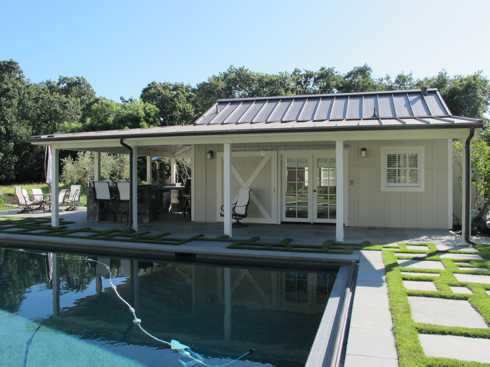 Modelo de casa de la piscina y piscina de estilo de casa de campo de tamaño medio rectangular en patio trasero con adoquines de hormigón
