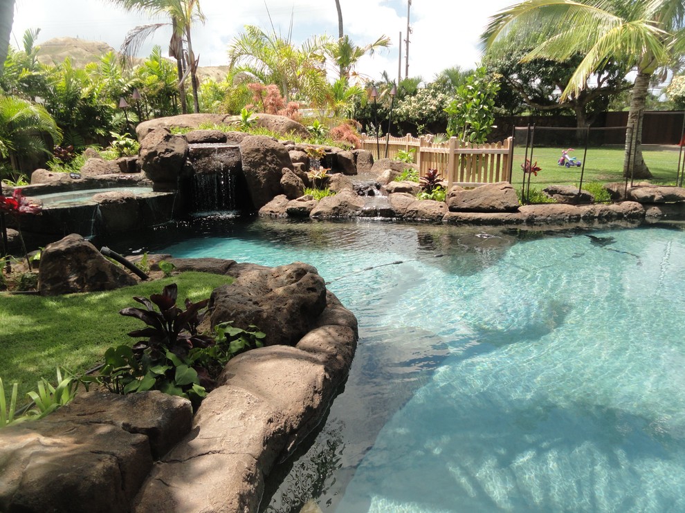 Ispirazione per una piscina tropicale personalizzata di medie dimensioni e dietro casa con pavimentazioni in pietra naturale e una vasca idromassaggio