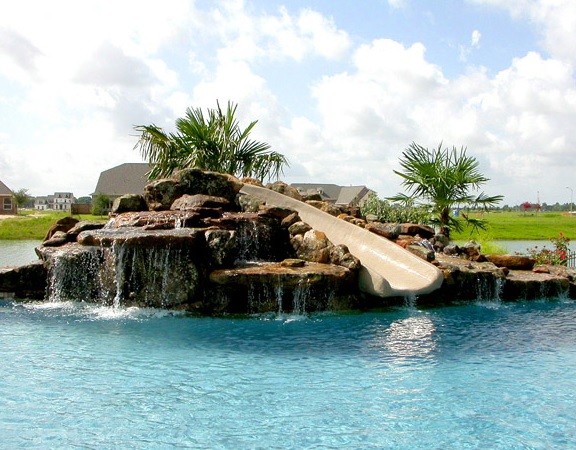 Ejemplo de piscina con tobogán tradicional grande a medida en patio trasero con suelo de hormigón estampado