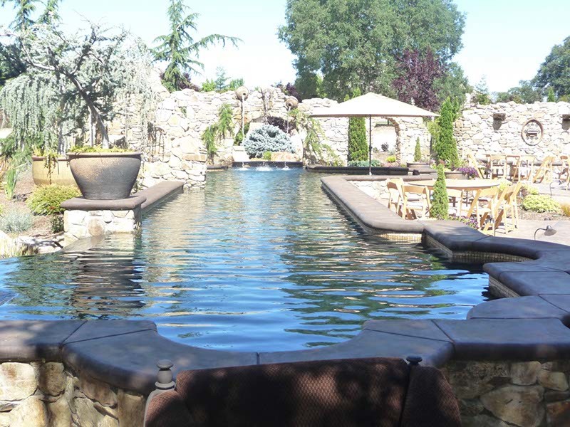 This is an example of a large traditional back custom shaped above ground swimming pool in Sacramento with natural stone paving and a water feature.