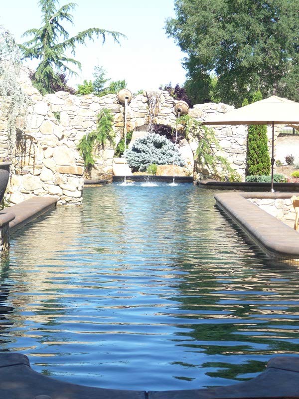 Ejemplo de piscina con fuente elevada tradicional grande a medida en patio trasero con adoquines de piedra natural