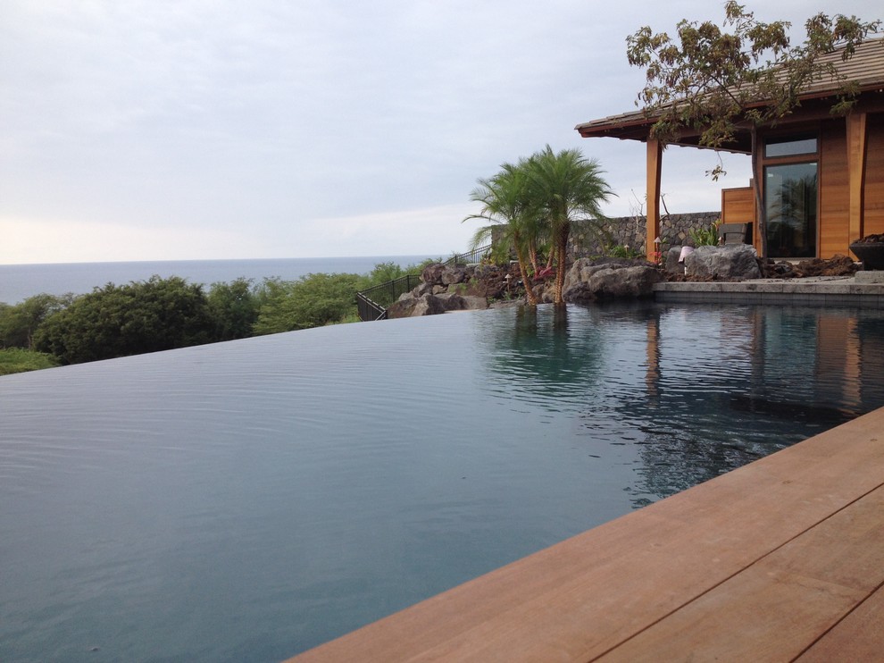 Esempio di una piscina a sfioro infinito tropicale personalizzata di medie dimensioni e dietro casa con una dépendance a bordo piscina e pavimentazioni in pietra naturale