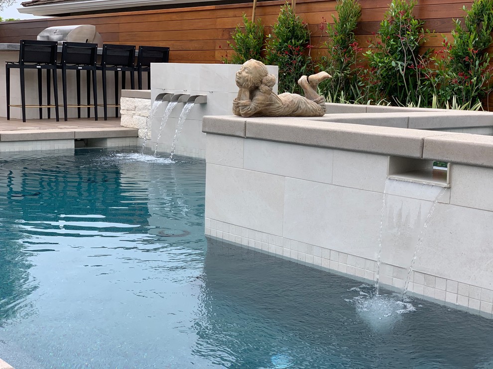 Ejemplo de piscina con fuente actual de tamaño medio en forma de L en patio trasero con adoquines de hormigón