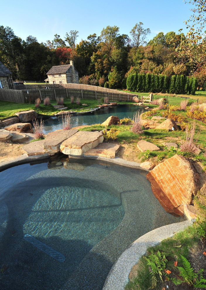Стильный дизайн: большой естественный бассейн произвольной формы на заднем дворе в стиле рустика с домиком у бассейна и покрытием из каменной брусчатки - последний тренд
