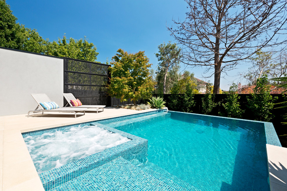 Ejemplo de piscina infinita contemporánea grande rectangular en patio trasero con adoquines de hormigón