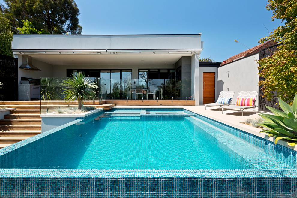 Modelo de piscina infinita moderna grande rectangular en patio trasero con adoquines de hormigón