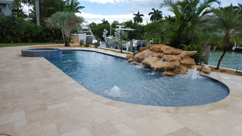 Exempel på en stor klassisk anpassad pool på baksidan av huset, med en fontän och naturstensplattor