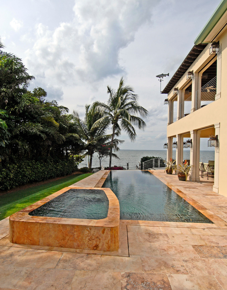 Ispirazione per una piscina a sfioro infinito tropicale rettangolare di medie dimensioni e dietro casa con una dépendance a bordo piscina e pavimentazioni in pietra naturale