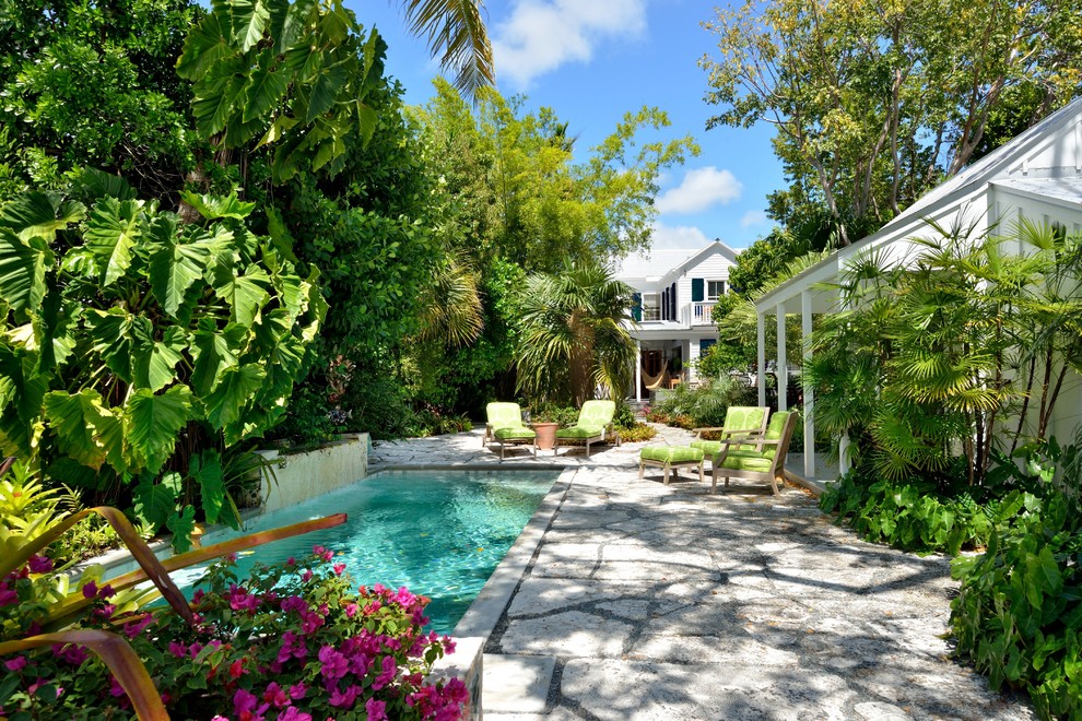 Imagen de casa de la piscina y piscina tropical rectangular en patio trasero con adoquines de hormigón