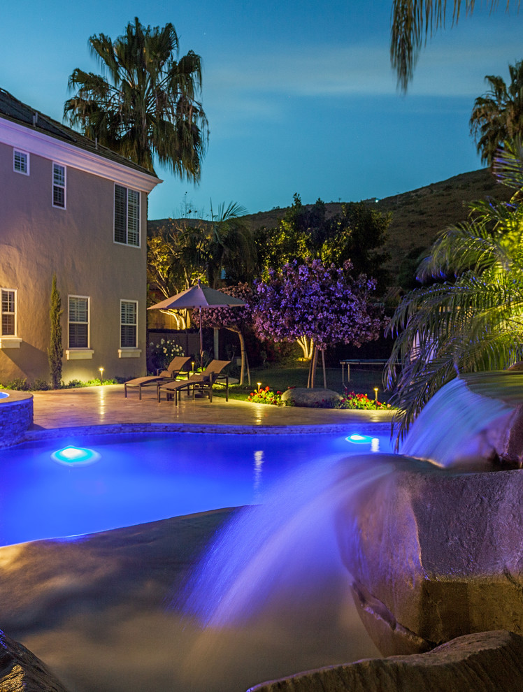 Esempio di una piscina tropicale personalizzata dietro casa con fontane e pavimentazioni in pietra naturale