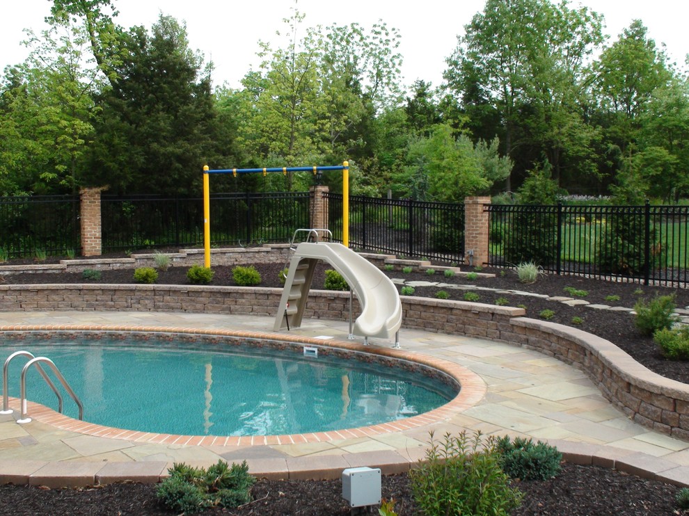 Immagine di una piscina classica a "C" di medie dimensioni e dietro casa con un acquascivolo e pavimentazioni in pietra naturale
