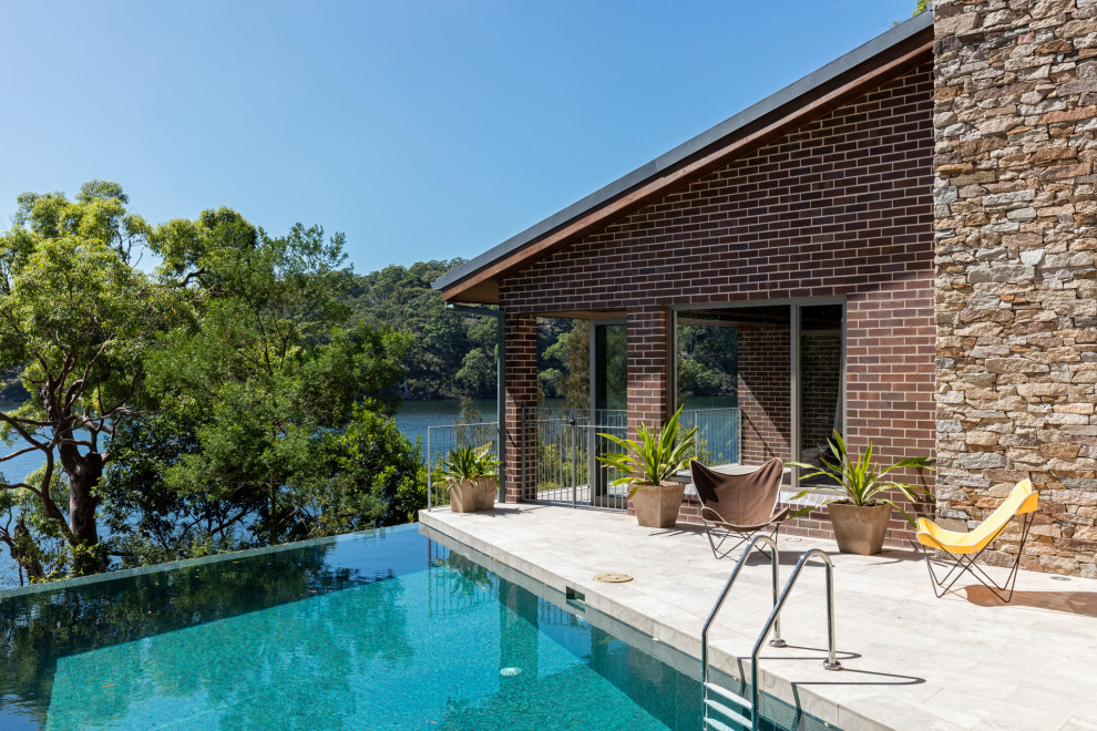 Ejemplo de piscina infinita vintage grande a medida en patio lateral con adoquines de piedra natural