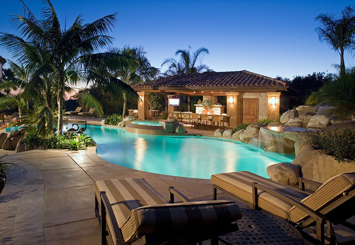 Idee per una grande piscina naturale tropicale personalizzata dietro casa con una vasca idromassaggio e lastre di cemento