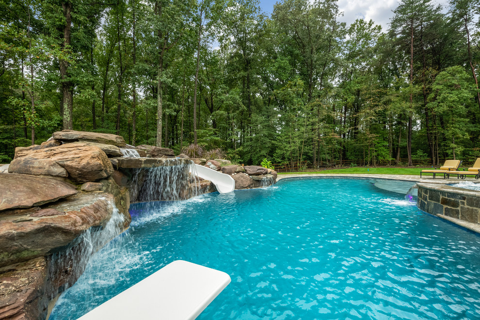 На фото: большой естественный бассейн в форме фасоли на заднем дворе в классическом стиле с водной горкой и покрытием из плитки с