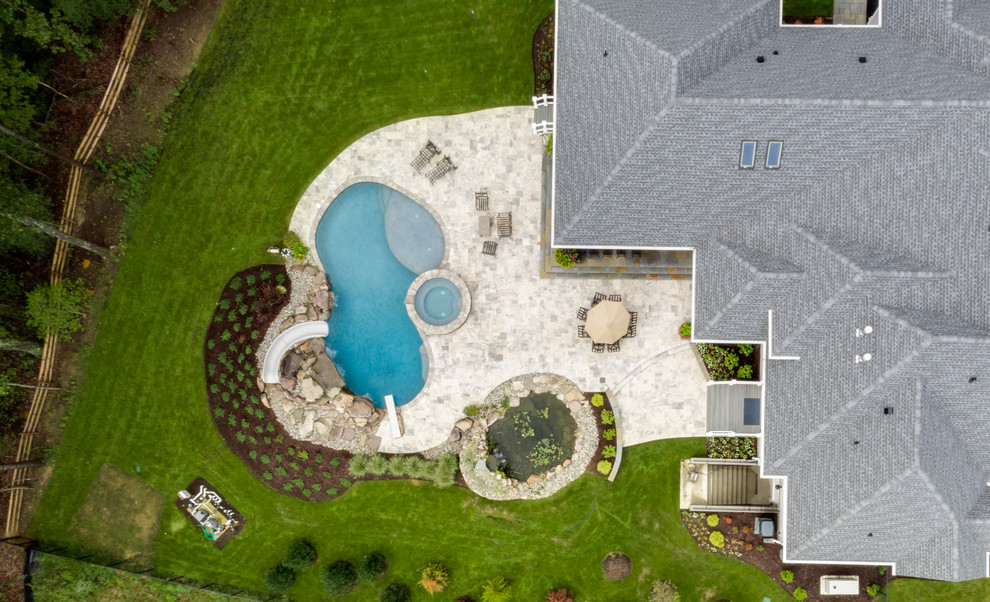 Ejemplo de piscina con tobogán natural clásica grande tipo riñón en patio trasero con suelo de baldosas