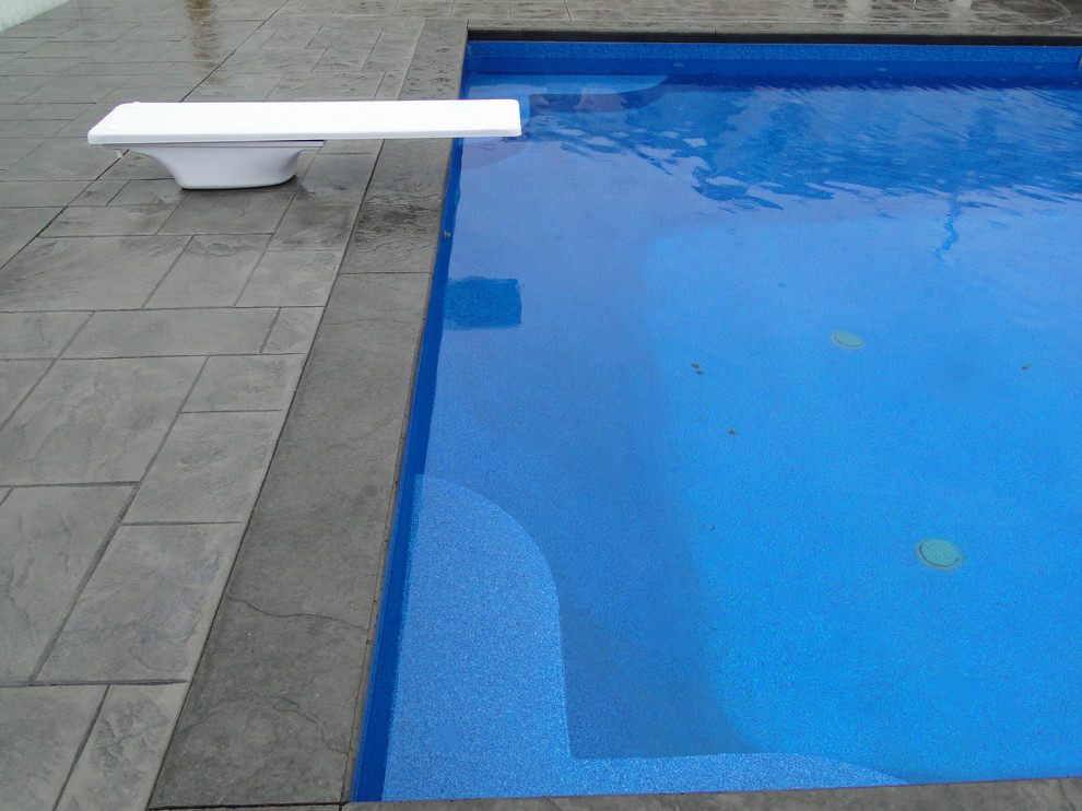 На фото: большой угловой бассейн на заднем дворе в стиле модернизм с покрытием из декоративного бетона