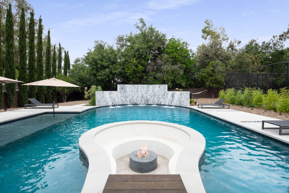 Immagine di un'ampia piscina naturale stile marinaro rettangolare dietro casa con fontane e lastre di cemento