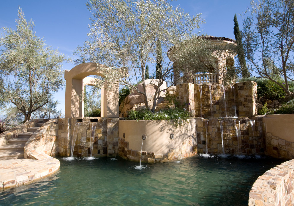 Foto de piscina con fuente alargada mediterránea grande a medida en patio trasero con adoquines de piedra natural