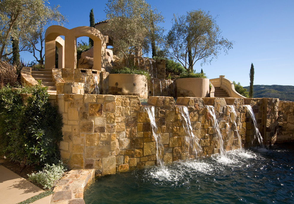 На фото: большой естественный бассейн произвольной формы на заднем дворе в средиземноморском стиле с фонтаном и покрытием из каменной брусчатки