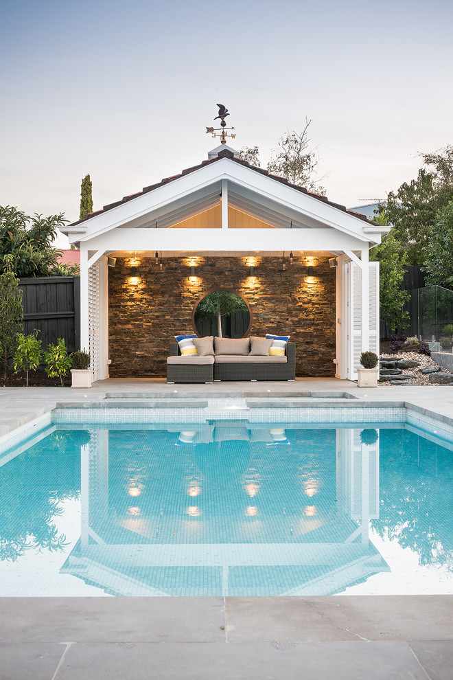 Modern inredning av en stor rektangulär pool på baksidan av huset, med poolhus och naturstensplattor