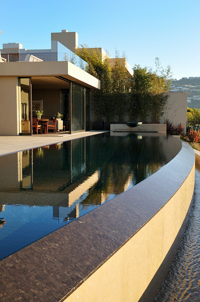 Ispirazione per una grande piscina a sfioro infinito design personalizzata dietro casa con fontane e pavimentazioni in pietra naturale