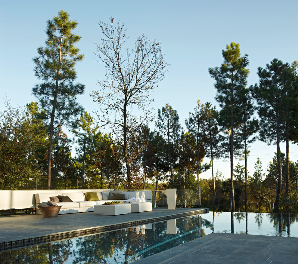 Imagen de piscina infinita actual grande en forma de L en patio trasero con adoquines de hormigón