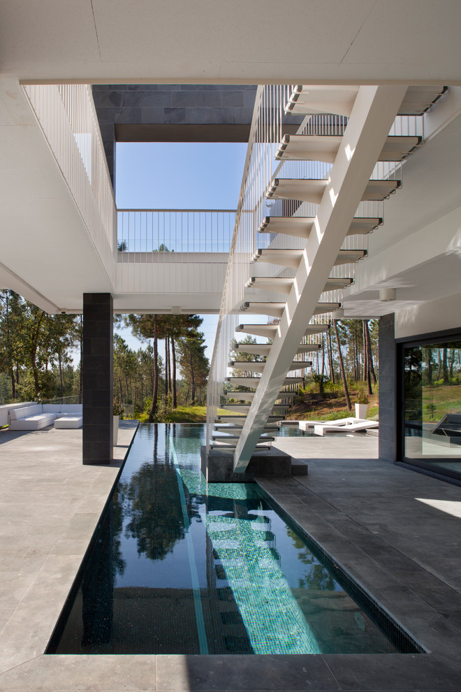 Esempio di una piscina a sfioro infinito design a "L" dietro casa e di medie dimensioni con pavimentazioni in cemento