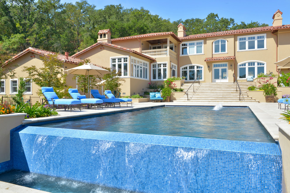 Ispirazione per una grande piscina monocorsia mediterranea rettangolare dietro casa con fontane e pavimentazioni in pietra naturale