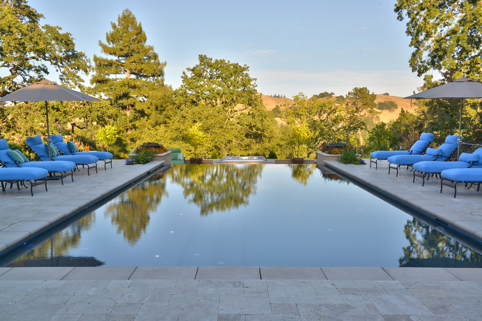 Immagine di una grande piscina monocorsia mediterranea rettangolare dietro casa con fontane e pavimentazioni in pietra naturale