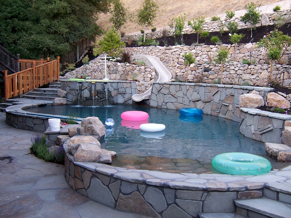 Inspiration för en mellanstor amerikansk njurformad baddamm på baksidan av huset, med vattenrutschkana och naturstensplattor
