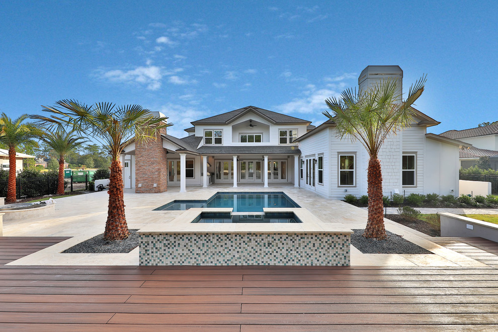 Foto di una grande piscina costiera a "L" dietro casa con pavimentazioni in pietra naturale e una vasca idromassaggio