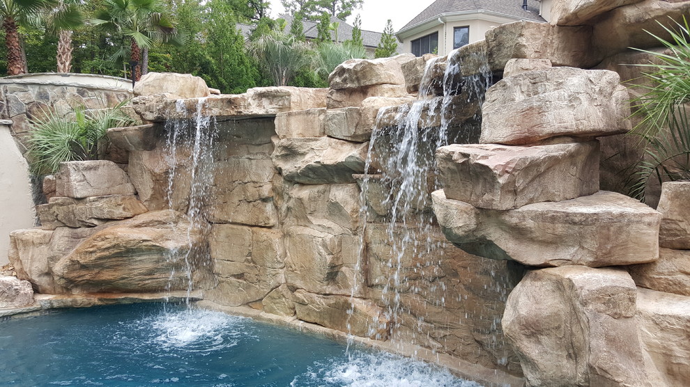 Bild på en stor tropisk anpassad pool på baksidan av huset, med vattenrutschkana och naturstensplattor