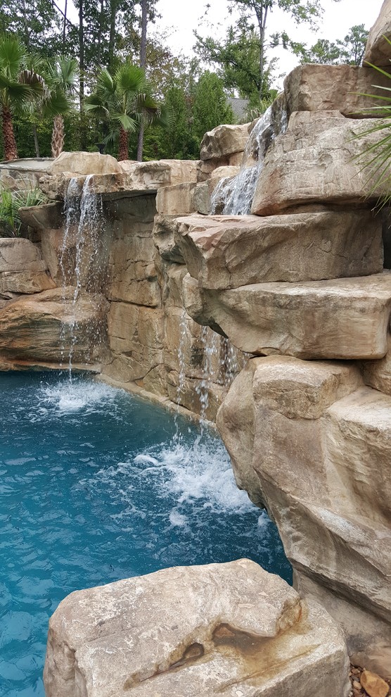 Ejemplo de piscina con tobogán exótica grande a medida en patio trasero con adoquines de piedra natural