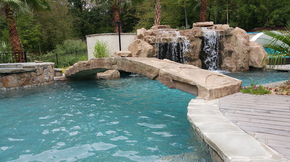 Idee per una grande piscina tropicale personalizzata dietro casa con un acquascivolo e pavimentazioni in pietra naturale