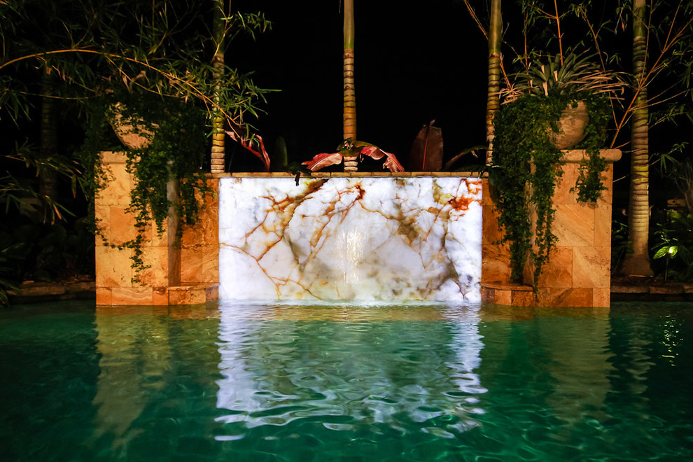 Esempio di un'ampia piscina monocorsia tropicale personalizzata dietro casa con fontane e pavimentazioni in pietra naturale