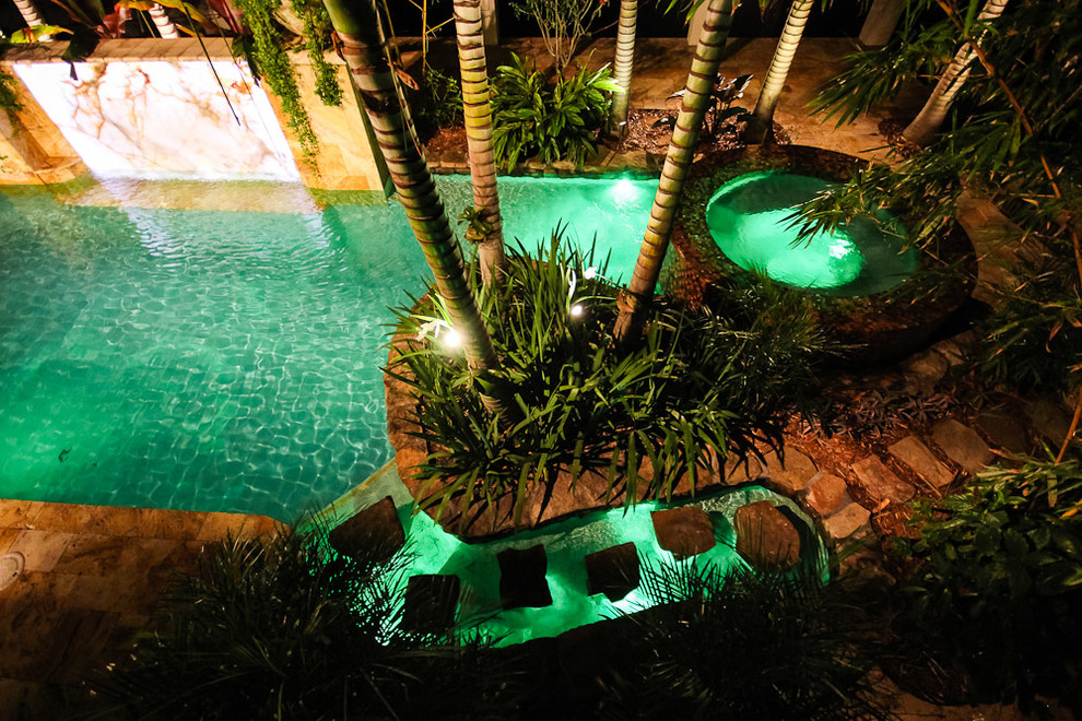 This is an example of an expansive world-inspired back custom shaped lengths swimming pool in Miami with a water feature and natural stone paving.