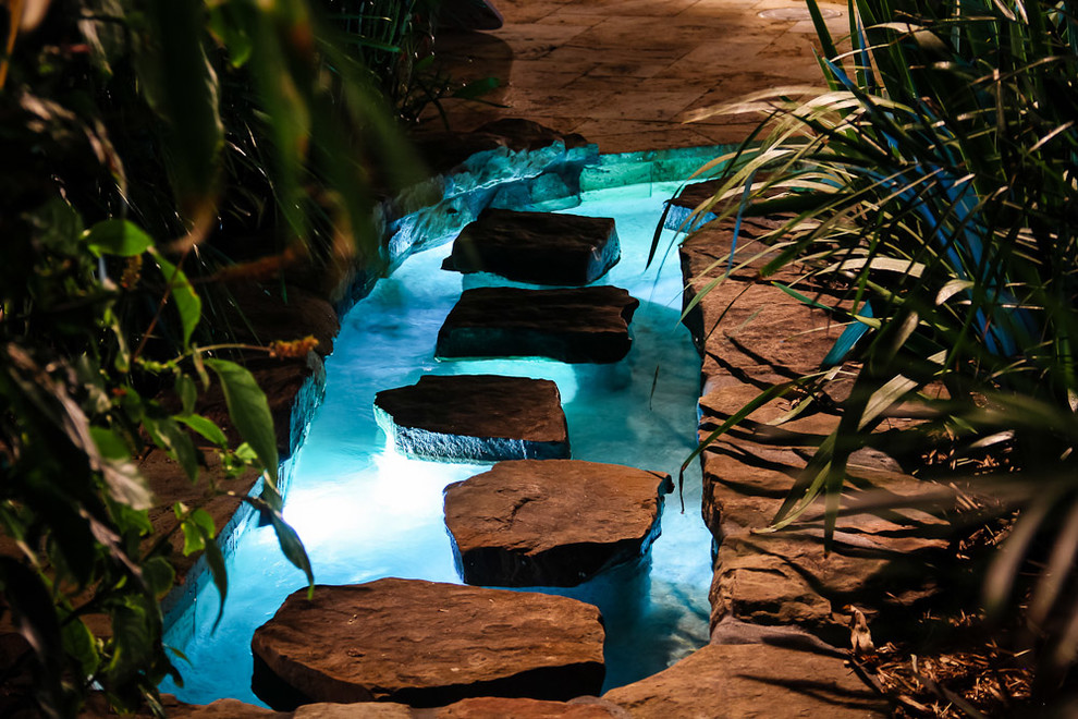 Ejemplo de piscina con fuente alargada tropical extra grande a medida en patio trasero con adoquines de piedra natural