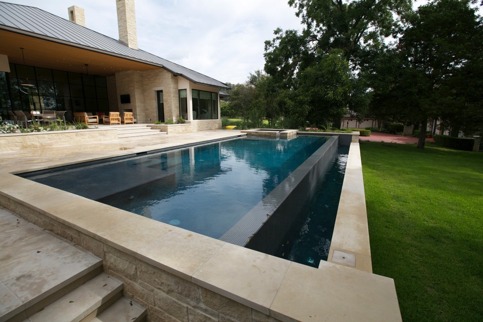 Ispirazione per una grande piscina a sfioro infinito design rettangolare dietro casa con fontane e pavimentazioni in pietra naturale