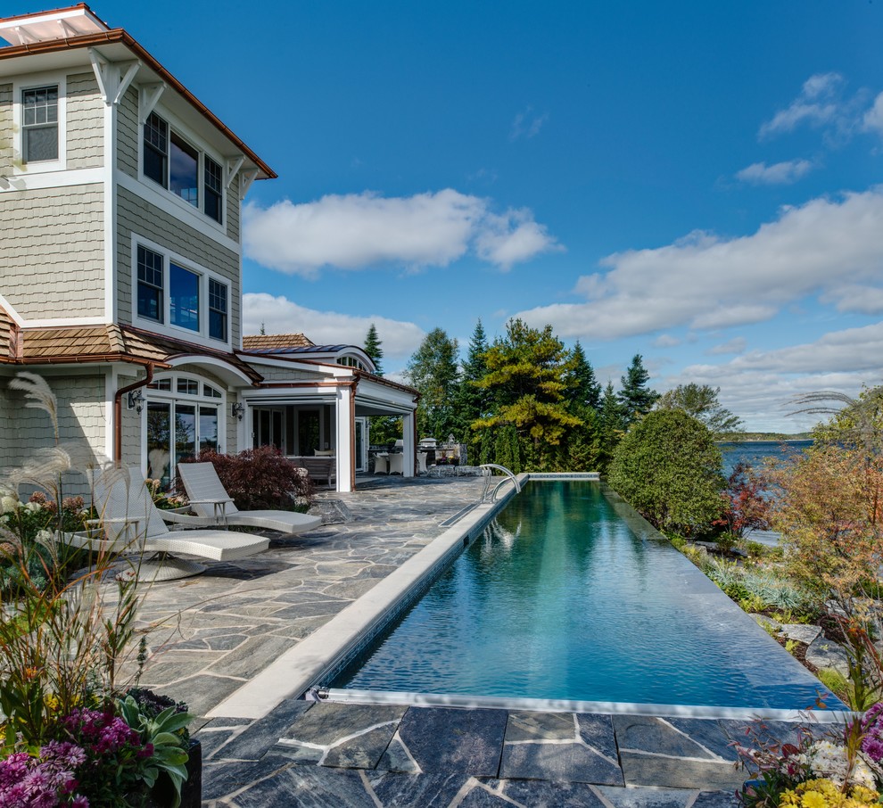 Immagine di una grande piscina a sfioro infinito costiera rettangolare dietro casa con pavimentazioni in pietra naturale