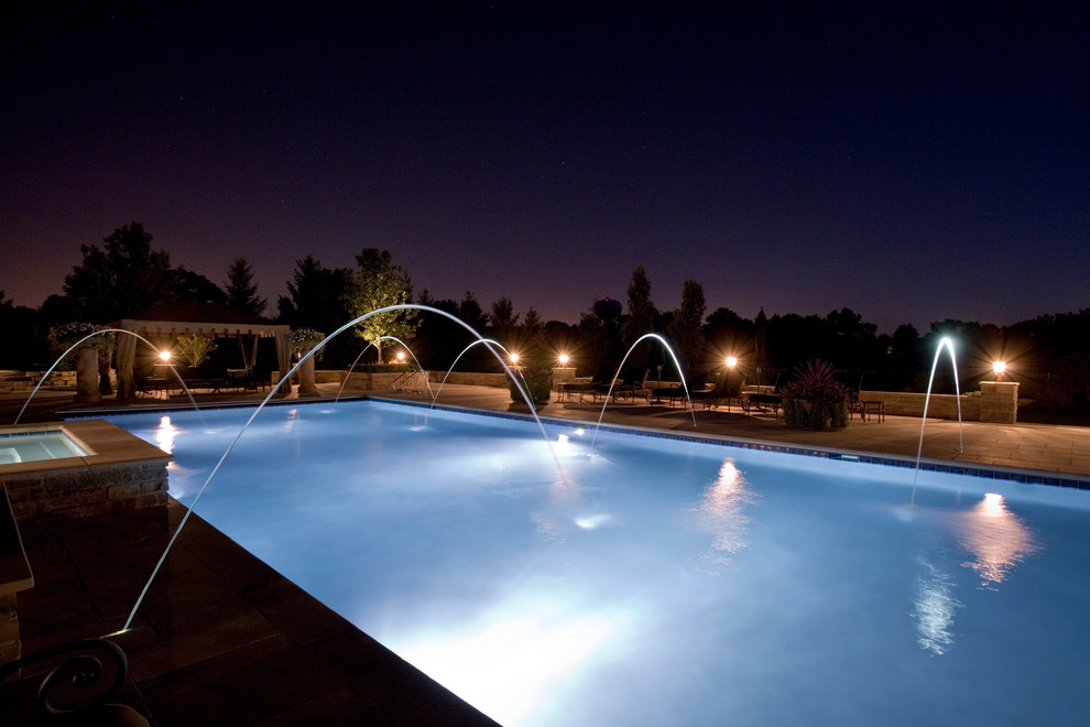 Ispirazione per una grande piscina monocorsia tradizionale rettangolare dietro casa con una vasca idromassaggio e pavimentazioni in pietra naturale