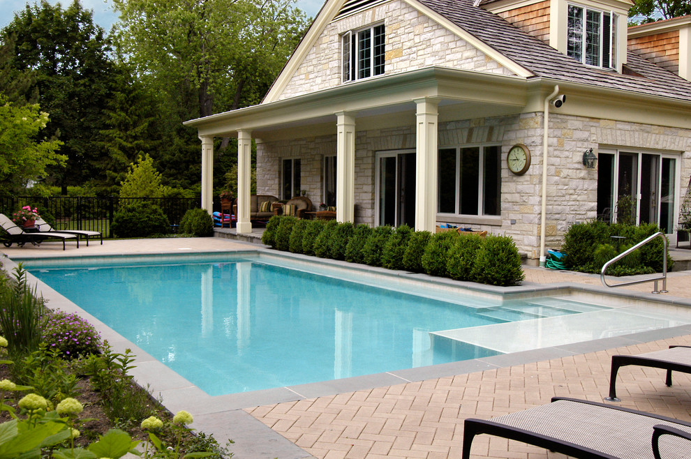 Ejemplo de piscina alargada tradicional pequeña en forma de L en patio lateral con adoquines de hormigón