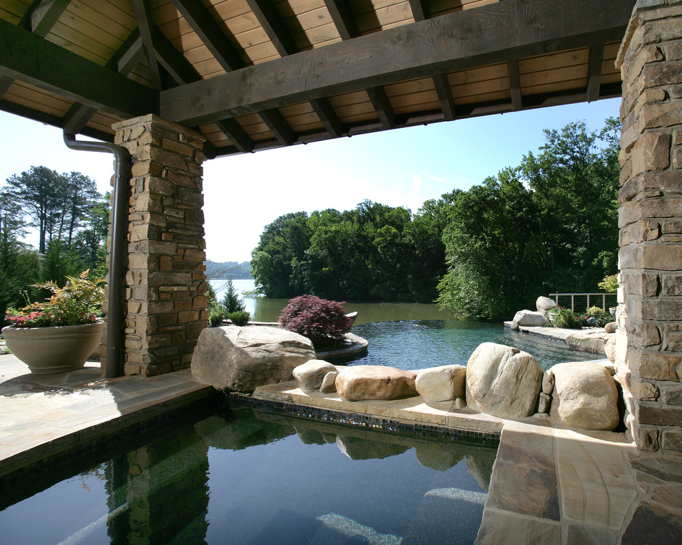 Ispirazione per una grande piscina a sfioro infinito tradizionale personalizzata dietro casa con una vasca idromassaggio e pavimentazioni in pietra naturale