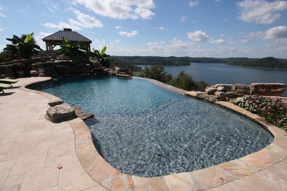 Immagine di una grande piscina a sfioro infinito stile marinaro personalizzata dietro casa con una vasca idromassaggio e pavimentazioni in pietra naturale