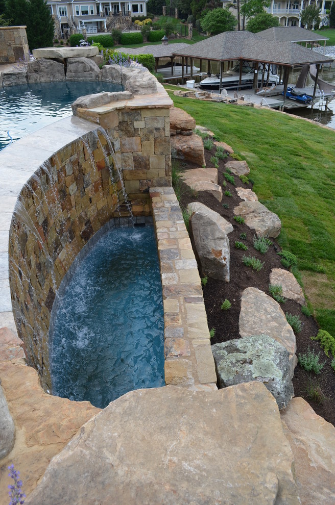 Réalisation d'une très grande piscine à débordement et arrière tradition sur mesure avec un point d'eau et des pavés en pierre naturelle.